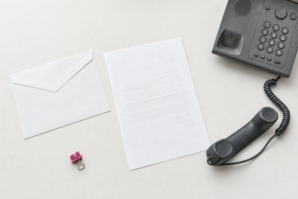 An unopened envelope and a face-down letter beside a telephone handset off its cradle