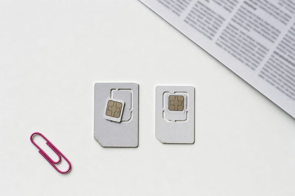 Two SIM cards on their punch-out carrier cards on a white desk, one chip snapped free of its frame, a printed sheet entering the corner of the frame