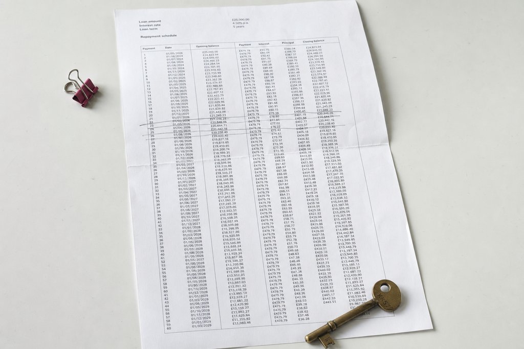 A folded printed repayment schedule with a brass key resting on the corner